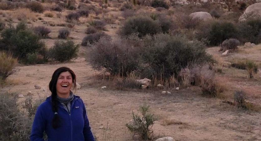 A person smiles at the camera amid a desert landscape